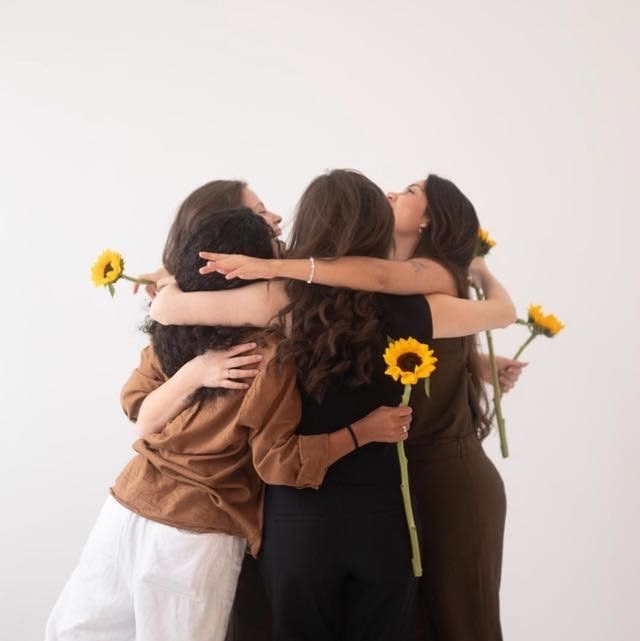 Mulheres se abraçando em roda segurando girassóis