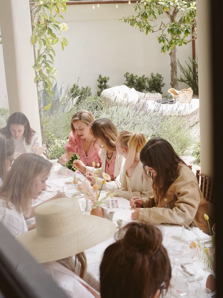 Mulheres reunidas em volta de uma mesa num jardim, pintando juntas